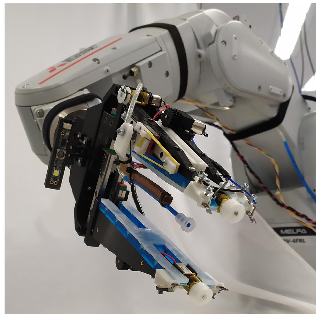 Fig. 1. The developed multi-modal robot gripper is equipped with < reconfigurable suction cup module that enables grasping of cables from flat surfaces without compromising the ability of the gripper to grasp other objects, dexterous tips that can manipulate the cables within the gripper, anc active Shape Memory Alloy based fingernails that can be used to pick uf objects from flat surfaces as well as for micromanipulation. The base of the proposed robotic gripper accommodates a camera that facilitates detection and pose estimation of flexible flat cables.  Joao Buzzatto, Jayden Chapman, Mojtaba Shahmohammadi, Felipe Sanches, Mahla Nejati, Saori Matsunaga, Rintaro Haraguchi, Toshisada Mariyama, Bruce MacDonald, and Minas Liarokapis 