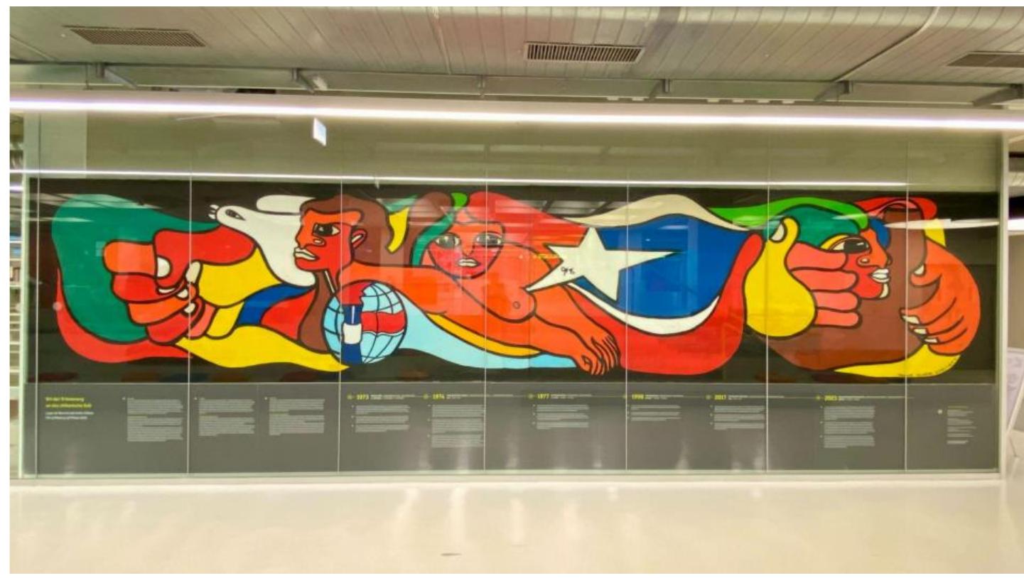 The mural at the University of Konstanz (figure 2) was painted by the Brigade Salvador Allende on 25 April 1977, during a concert by the exiled folklore ensemble Quilapaytin and the local Chilean-German choir, Singegruppe, in the main Audimax auditorium (Quilapaytin, 1977). During Quilapaytn’s performance, the brigade painted the mural on two canvases, which together measured 1.70m by 8.10m. At the end of the performance, the mural was hung on the wall opposite the Audimax, where it remained for more than four decades. It figuratively represents the global struggle for freedom of the Chilean people, personified by a female figure with a bare chest, her floating hair forming the Chilean flag, and symbols such as the clenched, oversized fist, a white dove and  eee md eee  The initiative to create a Chilean mural at the University of Konstanz came from a group of Chileans in exile that arrived in Konstanz as early as July 1974, who had been assigned to work or study at the university: philosopher Eduardo Arancibia Délano, professor of statistics Alicia Dominguez Diaz, sociologist Mario Duran Vidal, biology teacher Maria Francisca Marin, lawyer Francisco Otey, professor of education Angel Pizarro, and doctoral student in chemistry, Benjamin Suarez Isla. They were supported by the local Chile Committee Konstanz, the general student’s committee Allgemeiner 