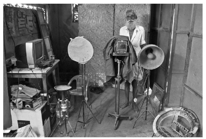 Image 6 Photographer Palaniappan. 2009.  Having started his own studio ‘Sathya Studios’ in 1965, Mr.Palaniappan, a photographer of yesteryears started his career in photography at the age of 17 taking guidance from his guru and helping him in printing and processing works, transferred his profession to his generation and had stopped working in the studio by 2002. He had started the studio with his old Yashica 12 that now he shows and boasts with pride. The dark room has lost its purpose as well. The studio, eventually, after taken over by his son turned into a digital one. And that gentleman’s resume reads this way-10th Class Pass, 2 months of training in Photoshop under his Uncle! Sadly, Palaniappan’s son deserted the studio for another job, while Palaniappan stands as a security in front of State Bank of India, Madurai branch. 