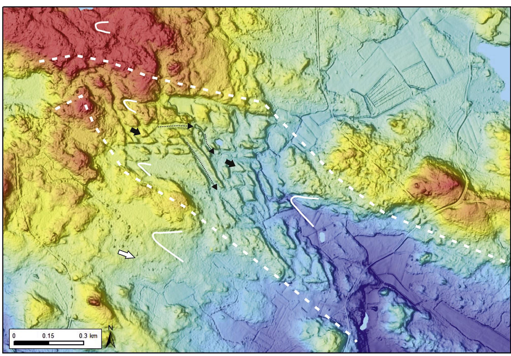 Fig. 4. The short Ylistenjarvi route (Fig. 2, site 10). The route shows mainly small triangular forms (short arrows) associated with small till ridges separated by channel-like passages (pointed arrows). The route goes across a bedrock high (in NW). Note the different fan-shaped hollows (solid curves); the ones outside the route with less erosional sides, whereas those within the route reveal sharper erosion. Colors indicate decreasing altitude from red (>100 m asl) to blue (<90 m asl). A white arrow shows the ice flow direction. Basemap and LiDAR © National Land Survey of Finland. LiDAR processing © Geologian tutkimuskeskus. 