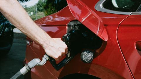 A hand holding a fuel pump filling up a red car.